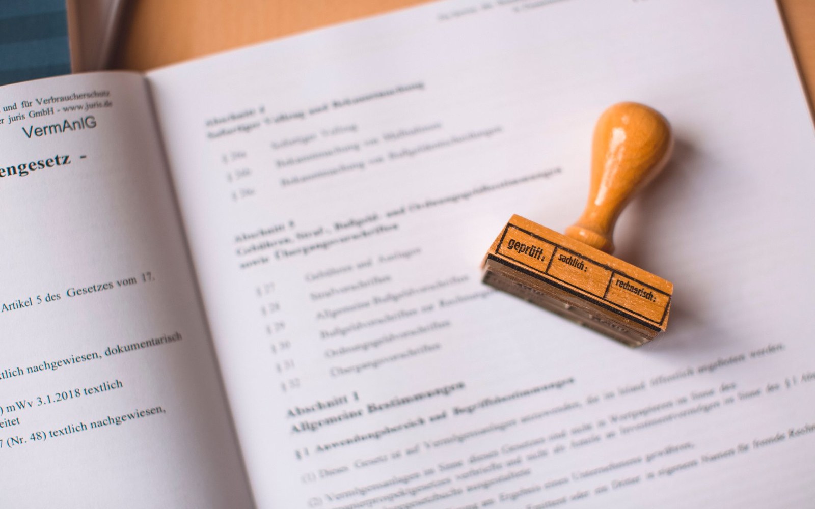 A wooden rubber stamp reading "geprüft" rests on an open German legal document