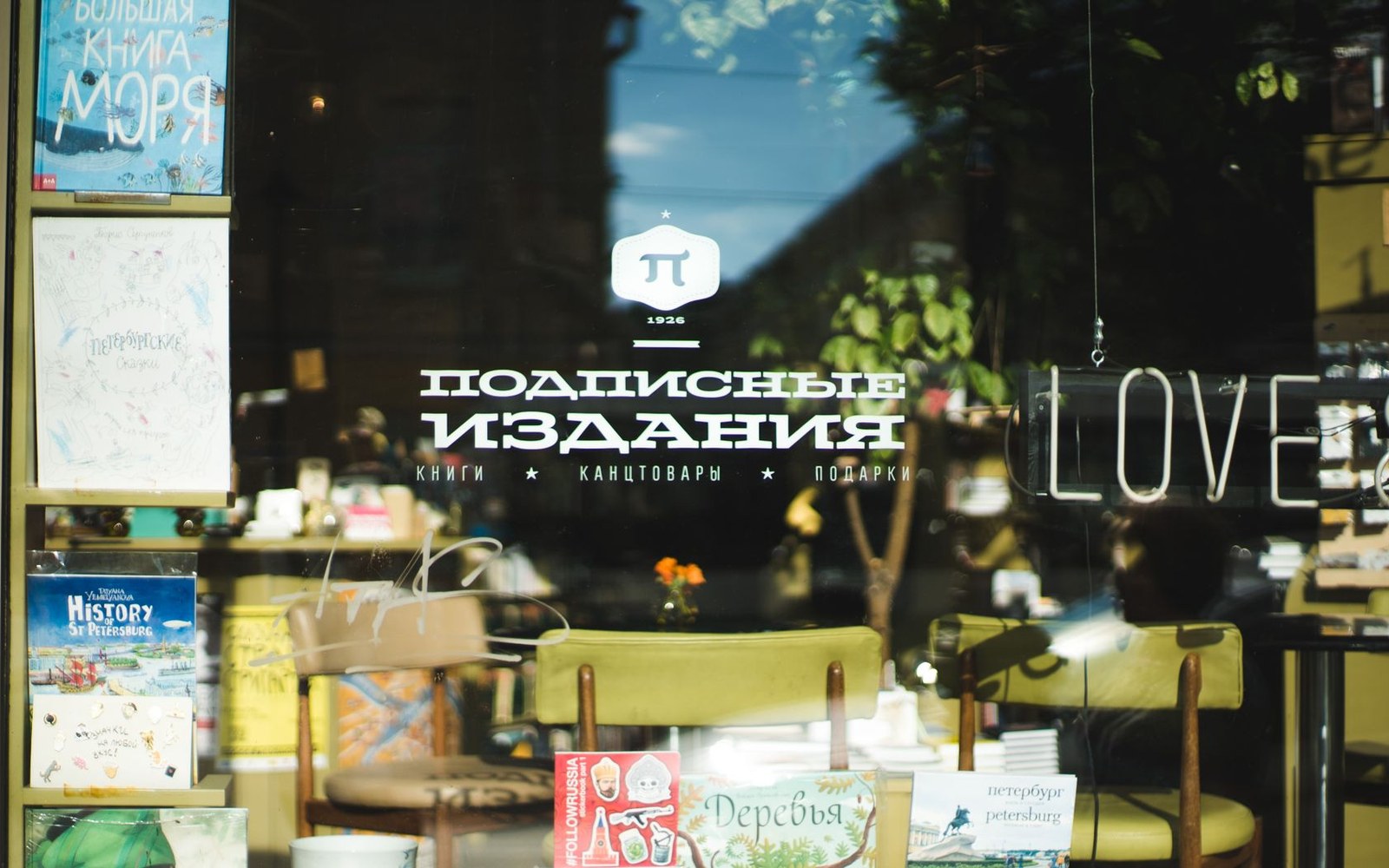 Bookstore storefront window with Cyrillic signage, displayed books, and a neon "love" sign
