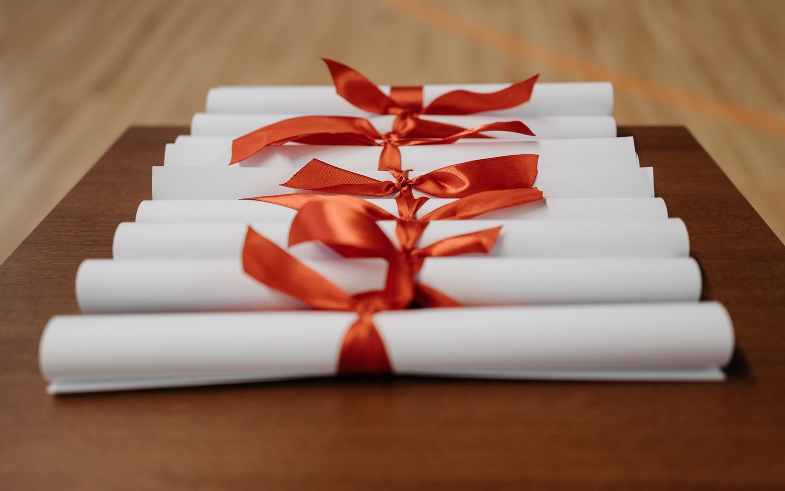 Rolled diploma-like scrolls tied with red ribbons stacked on a wooden table
