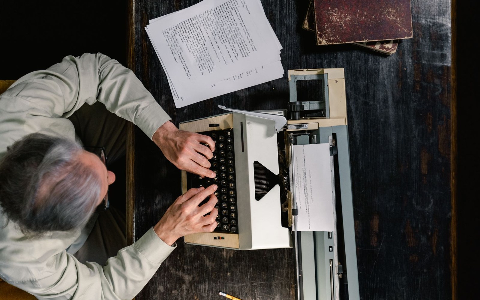 Overhead view of a man typing on a manual typewriter at a wooden desk