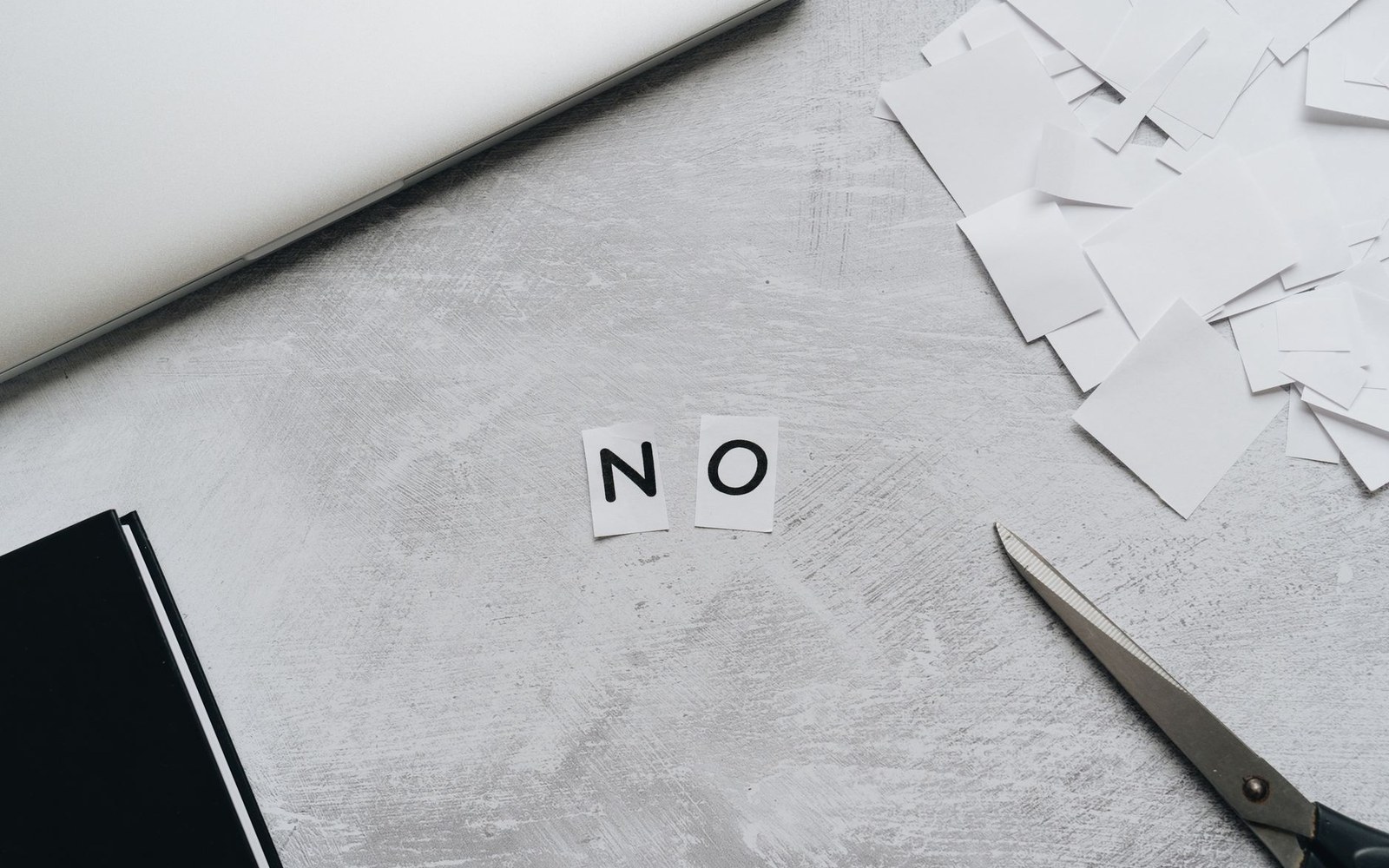 Cut-out paper letters spelling "no" on a desk with scissors and scraps