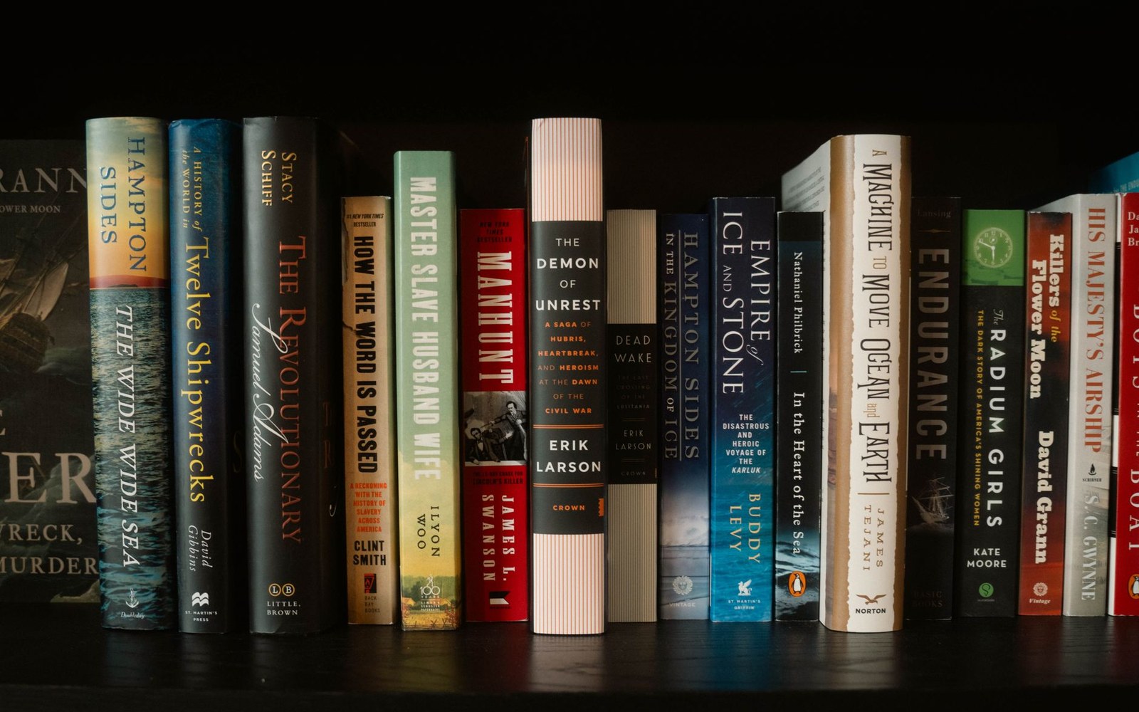 Rows of hardcover history books stand upright on a dark wooden shelf