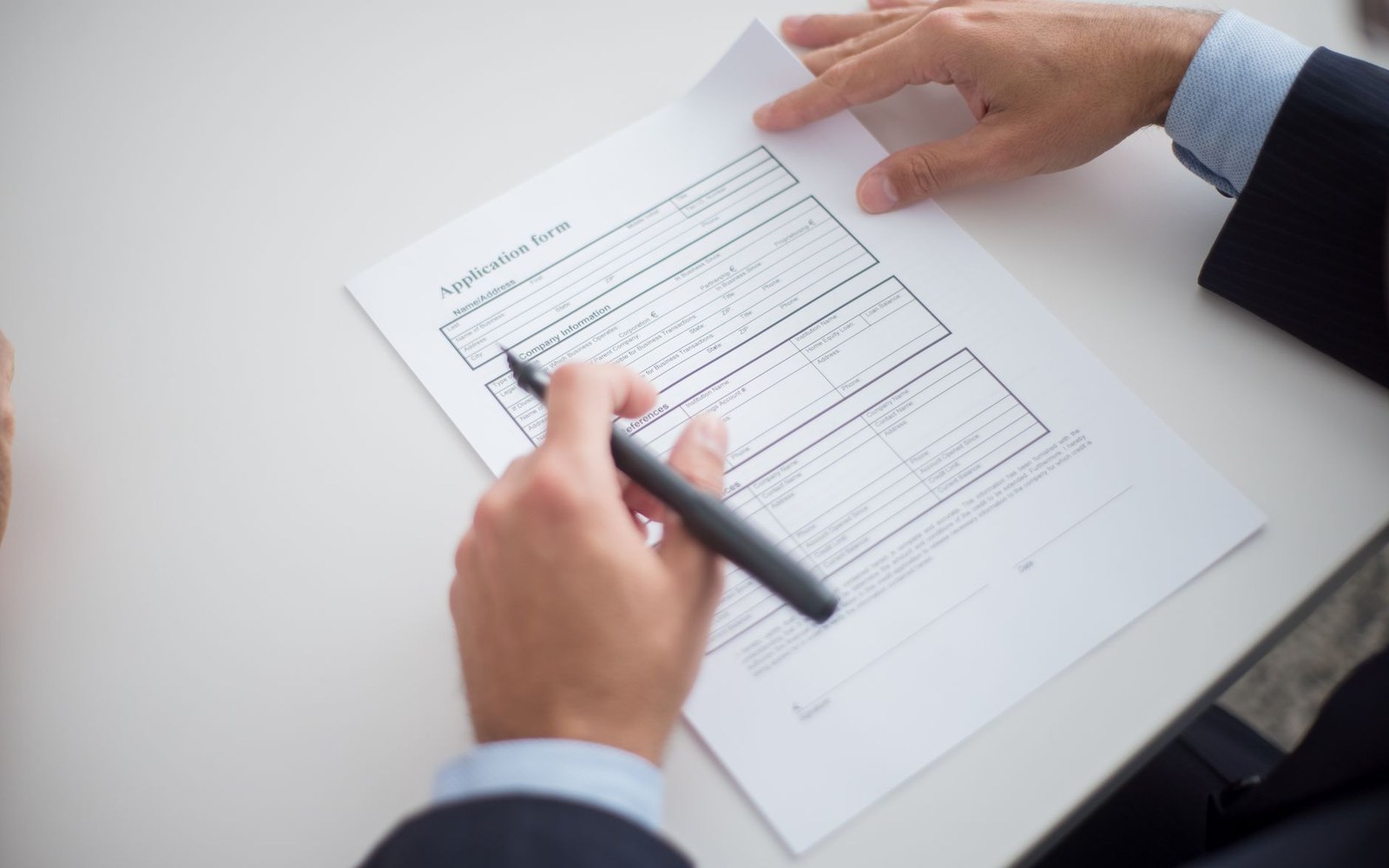 A man in a suit fills out a printed application form with a pen