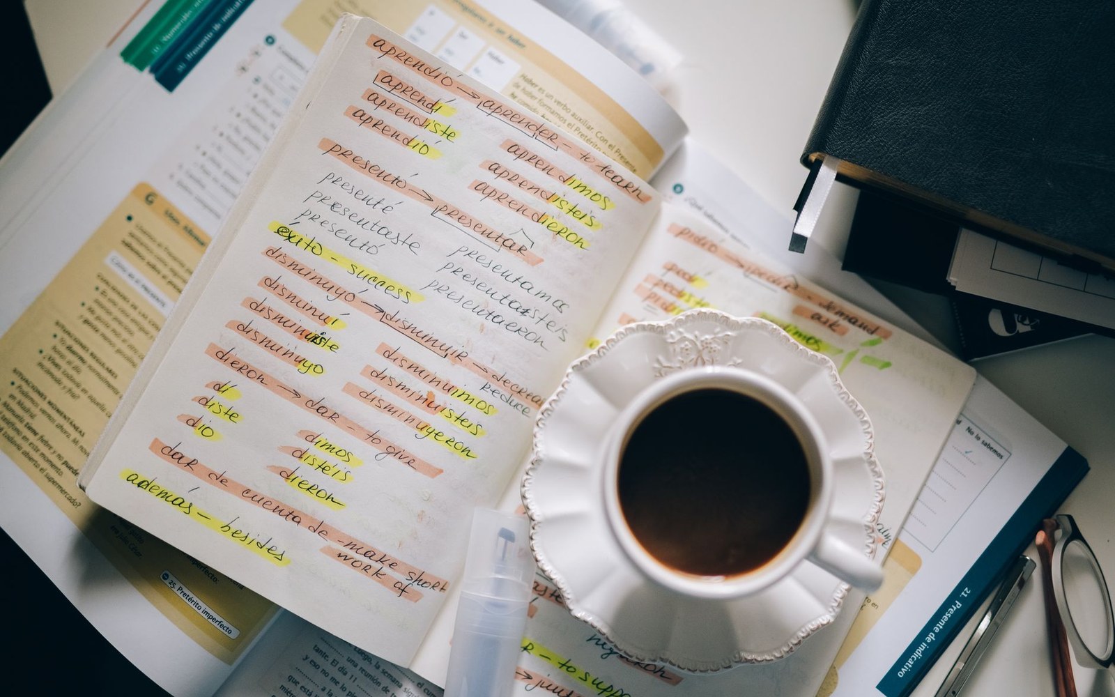 A cup of coffee sits beside a Spanish vocabulary notebook covered in highlighted verb conjugations