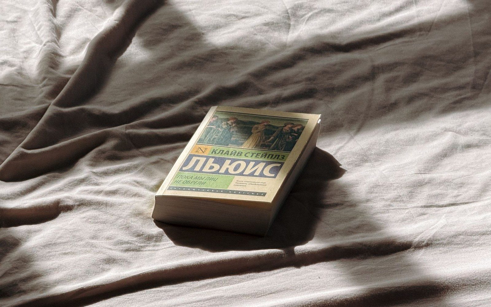 A paperback book by C.S. Lewis lying on wrinkled bedsheets in soft sunlight