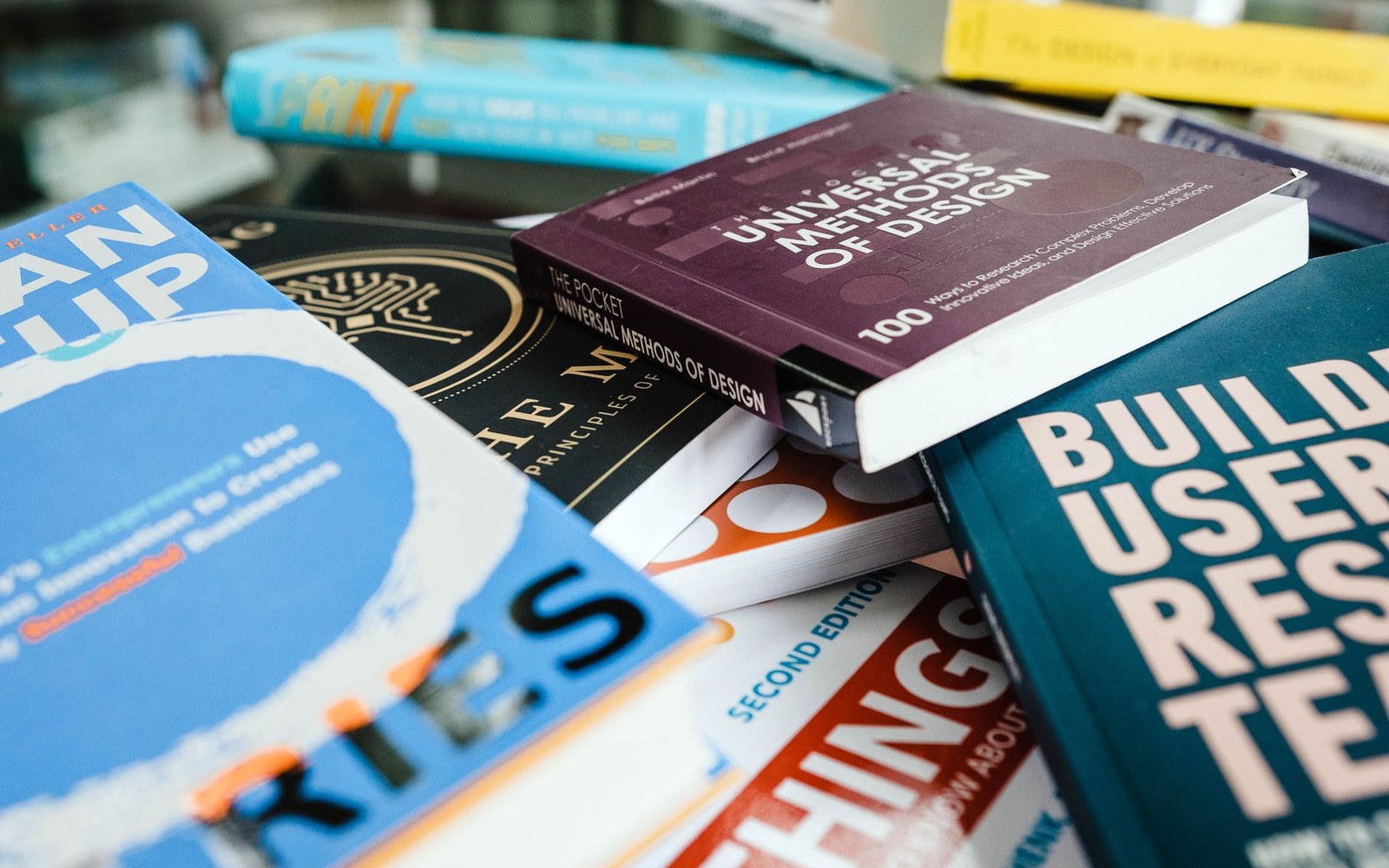 A cluttered stack of design and business books including Universal Methods of Design