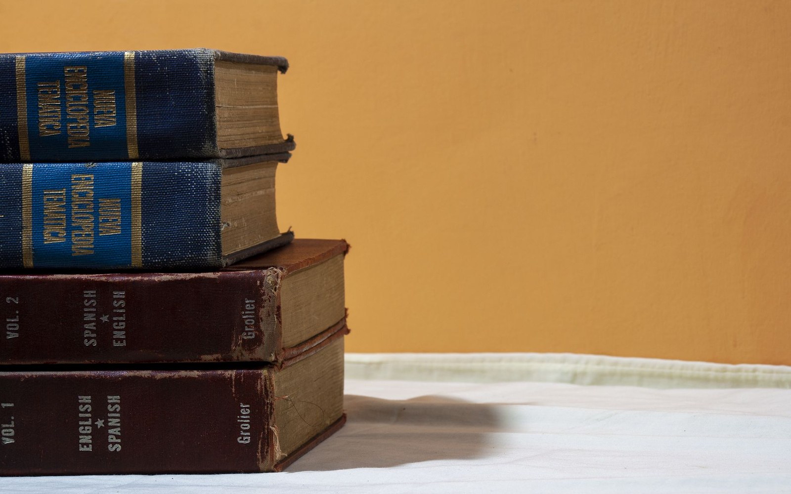 Stacked antique encyclopedia and bilingual Spanish-English dictionary volumes on a table